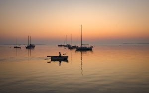 sailor in rowboat returns to shore in the evening