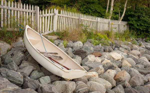 dinghy parked on rocky Maine seawall below a white picket fence