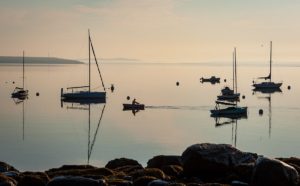 solitary sailor rows to his boat on still water early in the morning