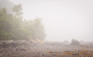 yellow kayak rests on a rocky beach on a foggy morning in Maine