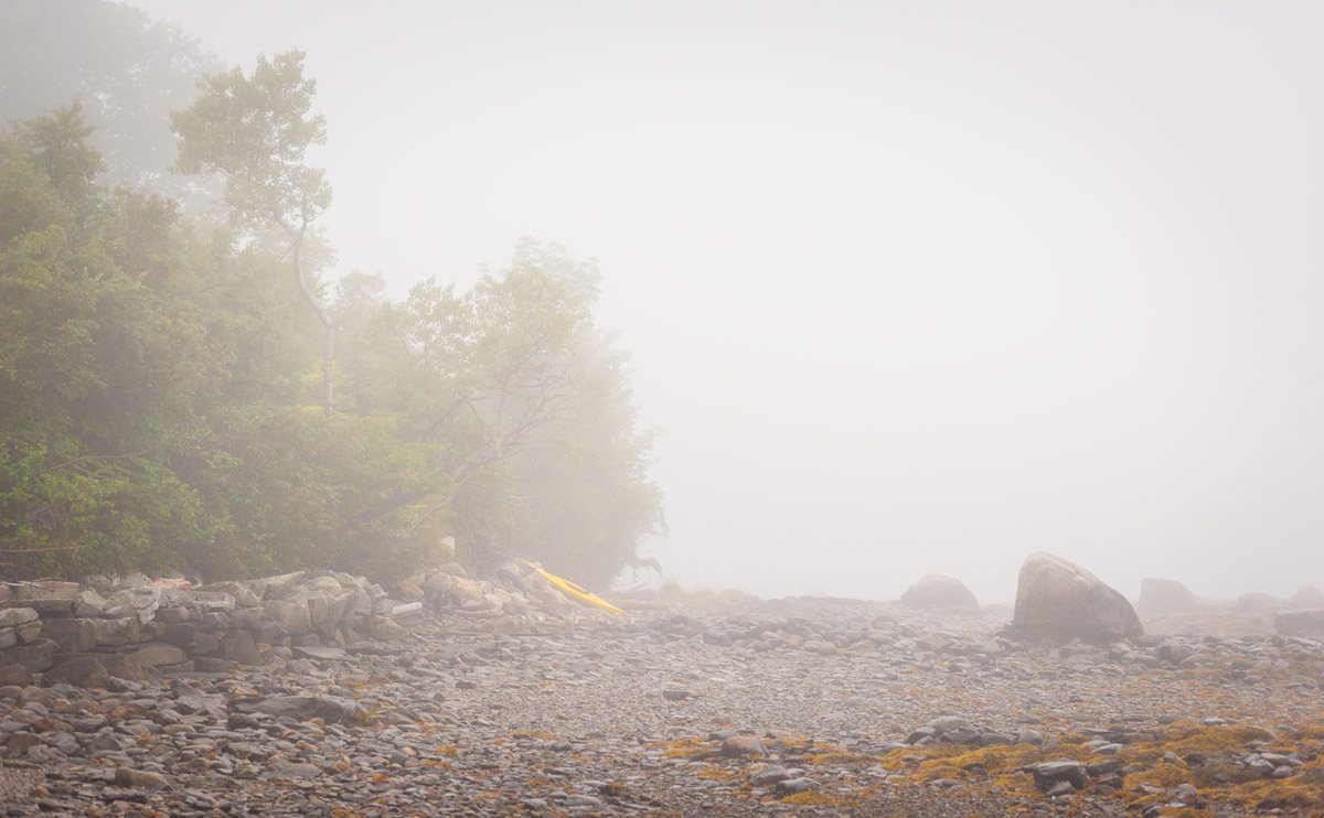 yellow kayak rests on a rocky beach on a foggy morning in Maine