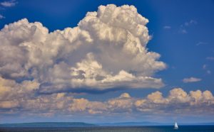 solitary sail boat beneath looming clouds